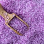 A wooden scoop is gently resting on top of purple bath salt.