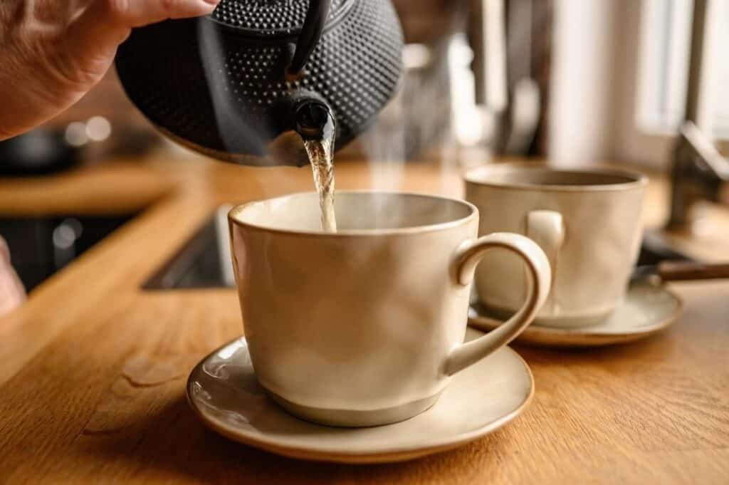 A person pouring tea into a cup on a wooden table.