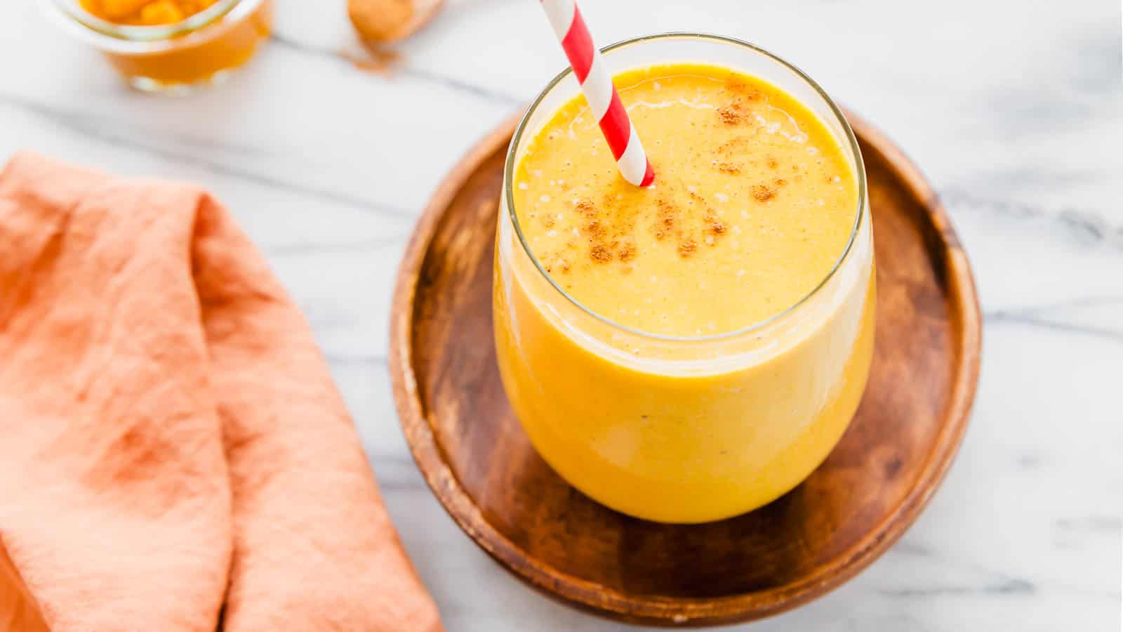 A glass of pumpkin banana smoothie with a straw in it.