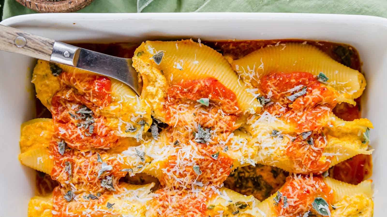 Pumpkin stuffed shells in a white dish with a spoon.