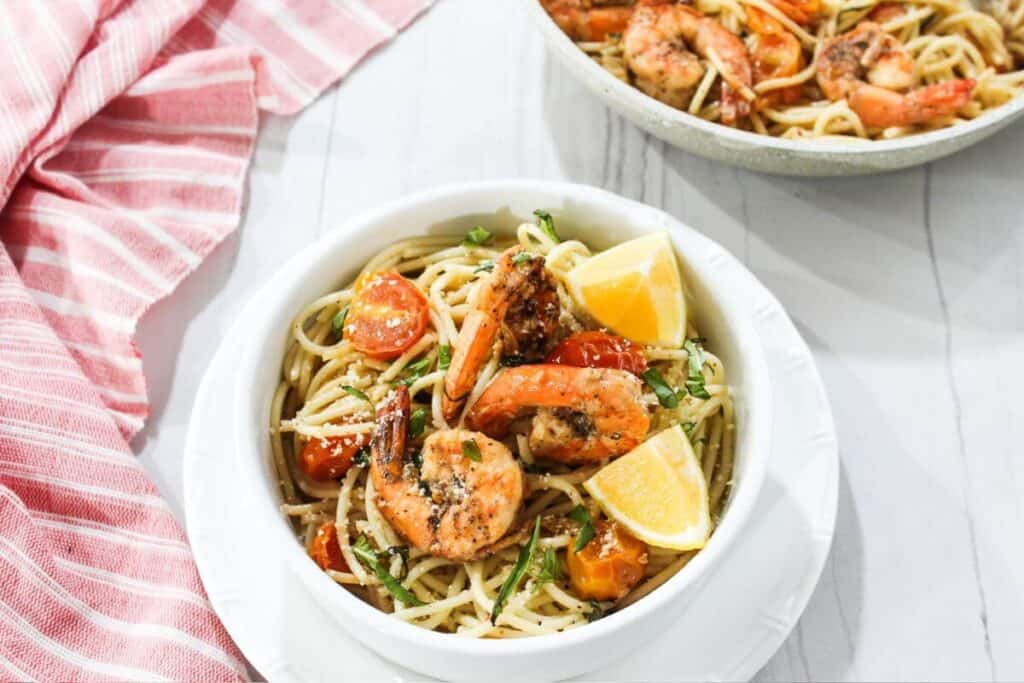 A bowl of pasta with shrimp and tomatoes.