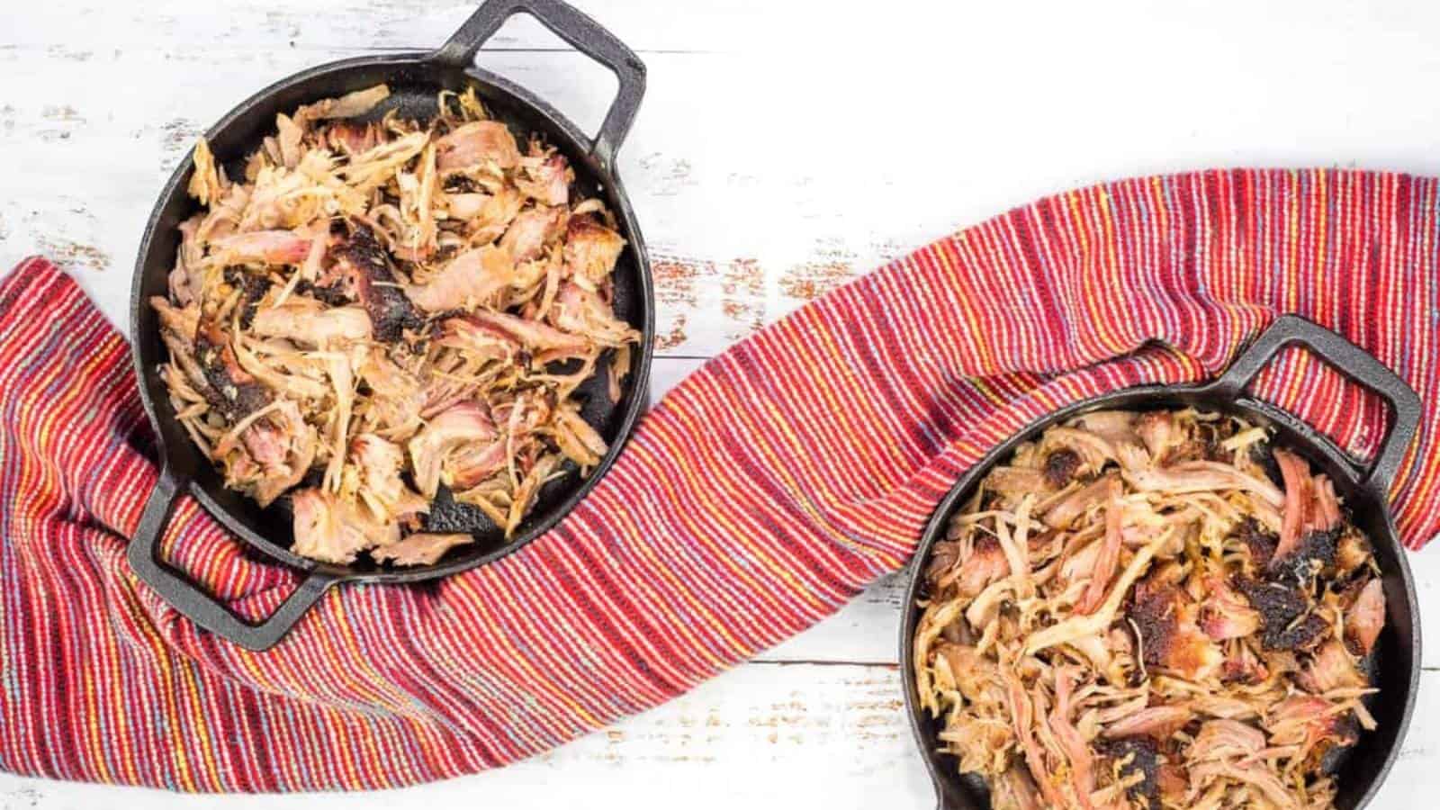 Two cast iron skillets with smoked pulled pork in them.