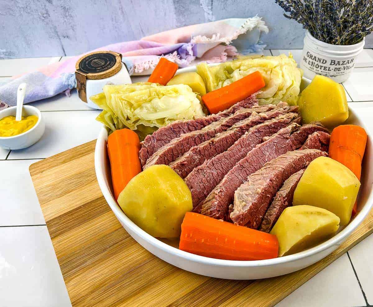 A bowl of corned beef and cabbage on a wooden cutting board with vegetables,