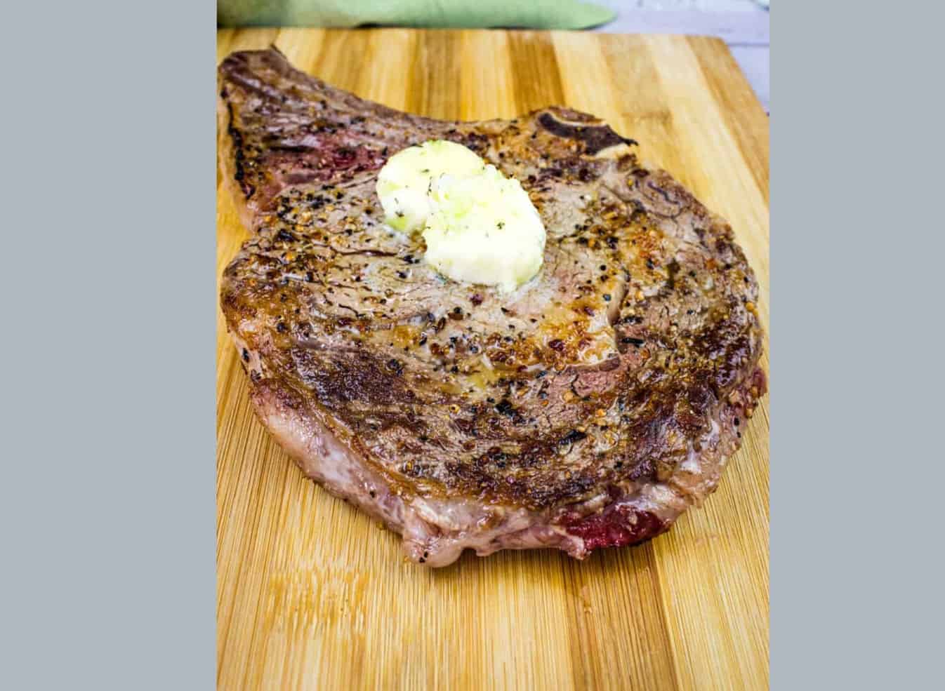 A steak on a cutting board with butter on it.
