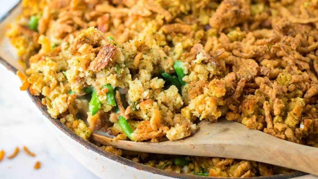 Green bean stuffing casserole in a baking dish with a wooden spoon.