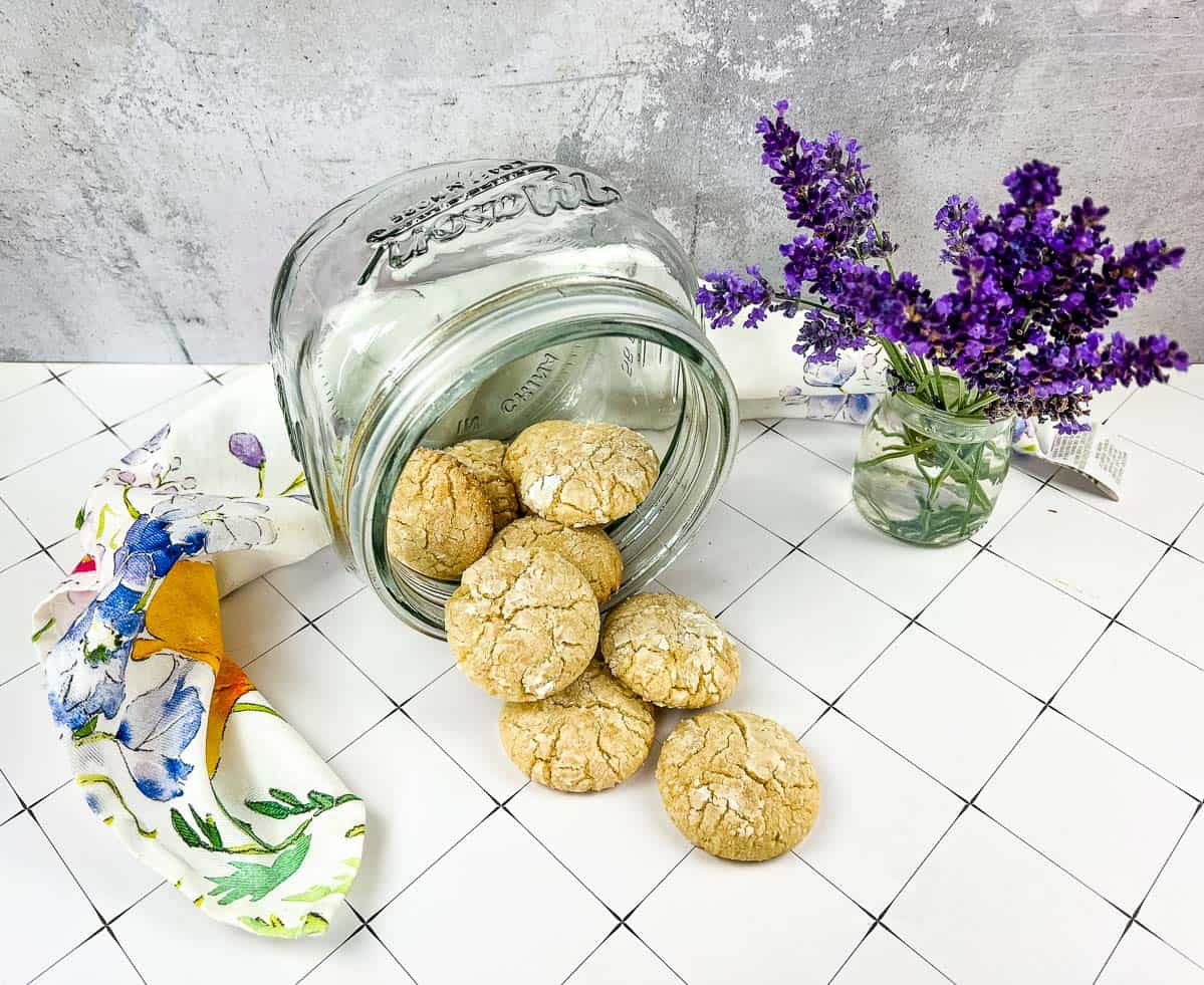 A jar of White Chocolate Crinkle Cookies next to lavender flowers.