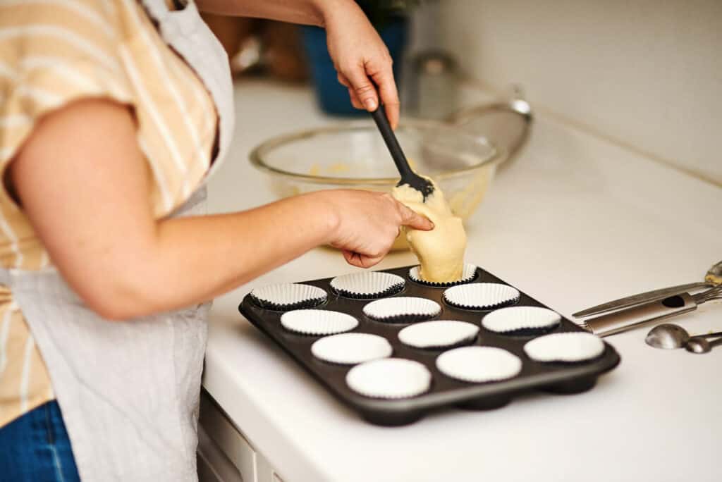 A woman spooning batter into a muffin tin.