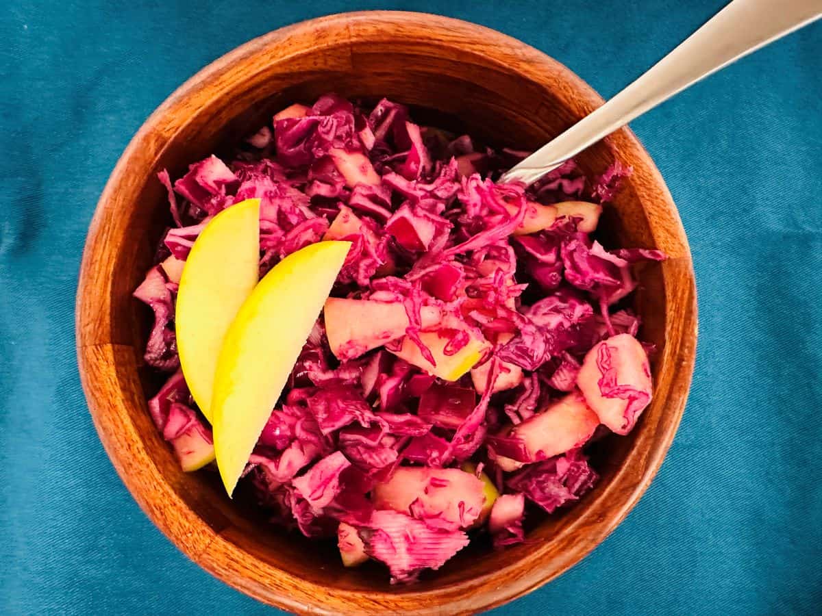 Red cabbage slaw in a wooden bowl with a spoon.