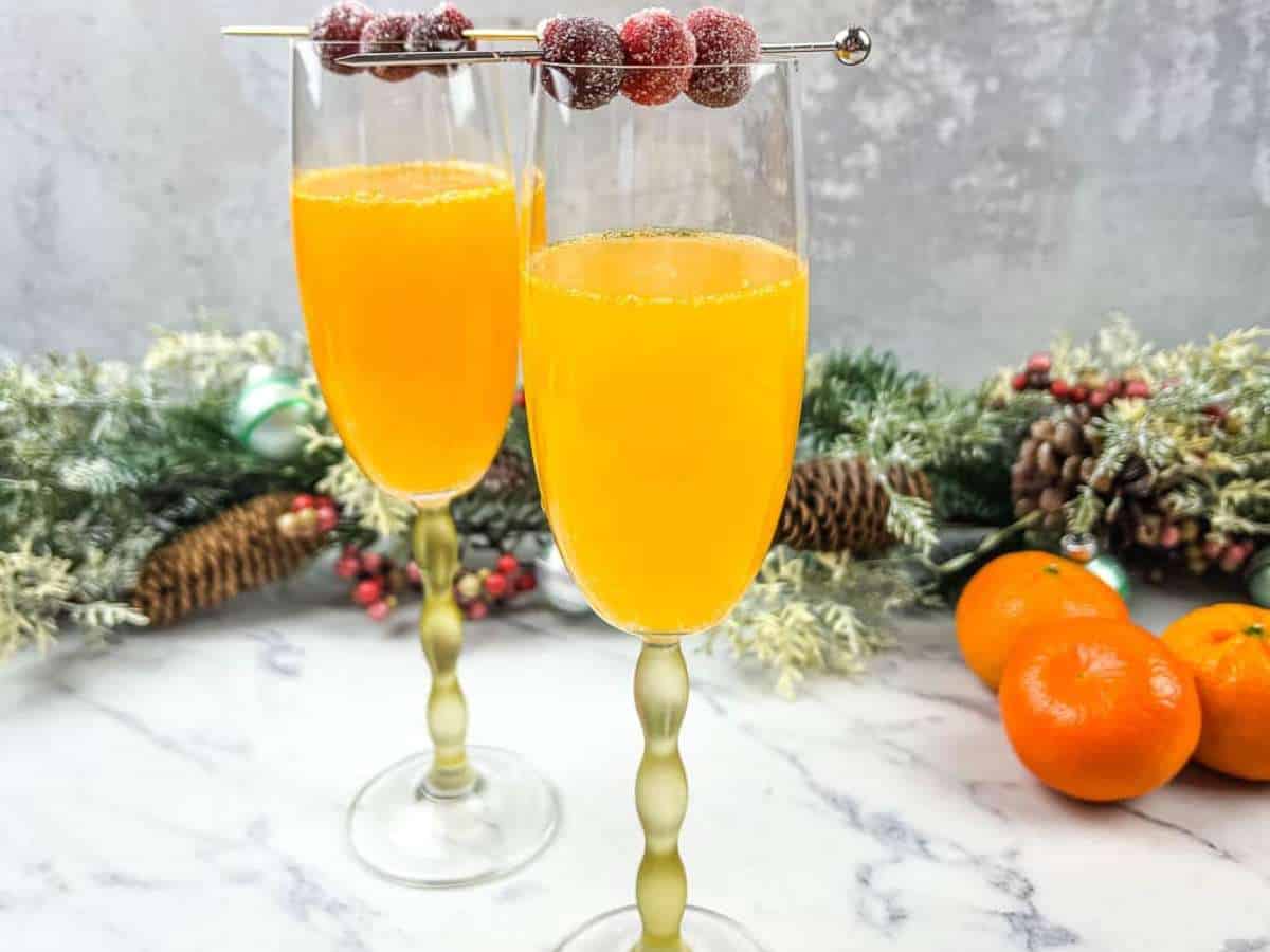 Two glasses of christmas mismosa with oranges and cranberries.