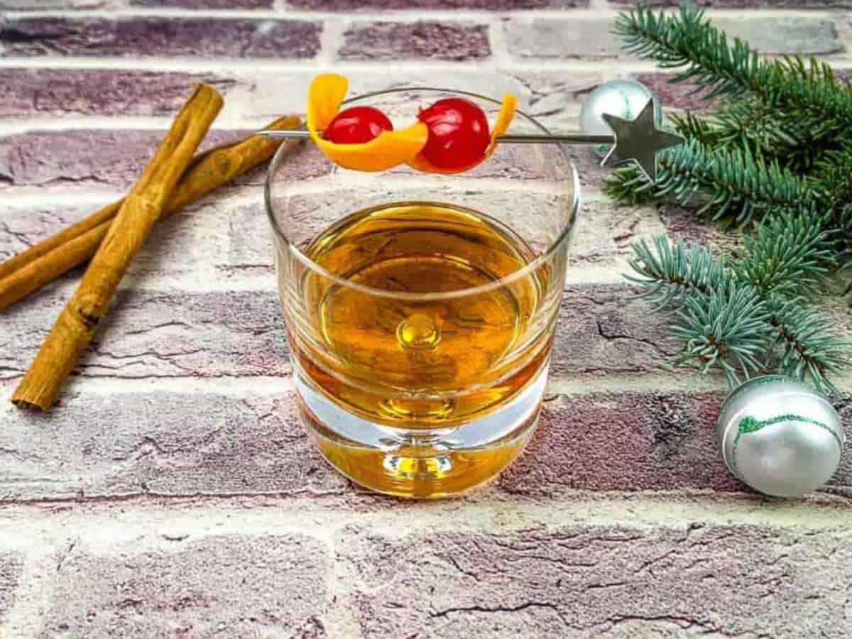 A glass of whiskey with cinnamon sticks on a brick wall.