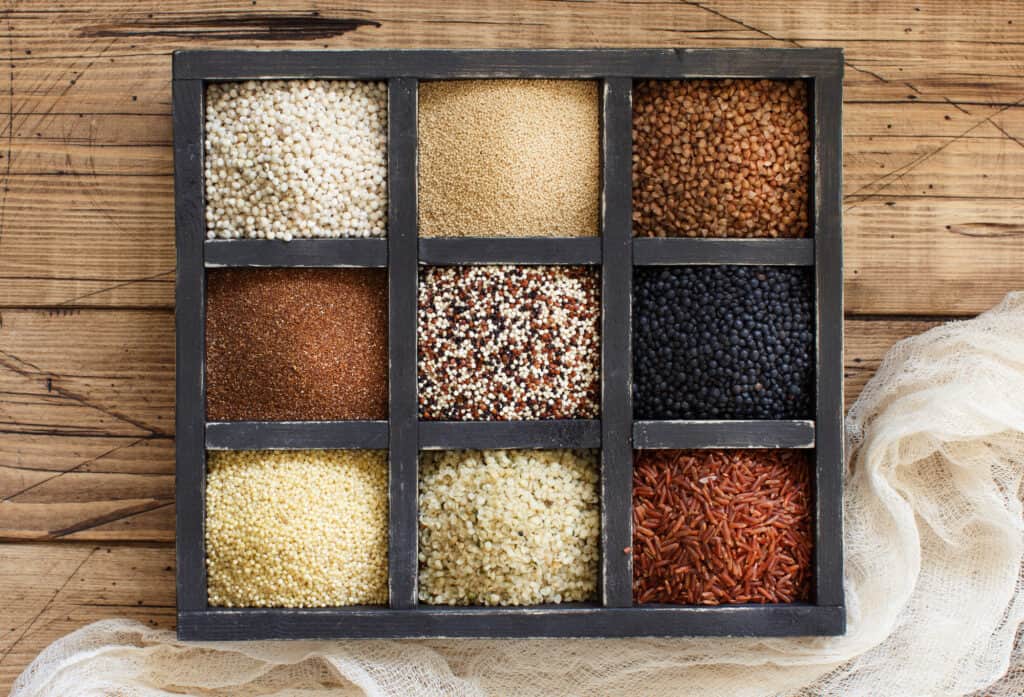 A box of different types of grains on a wooden table.