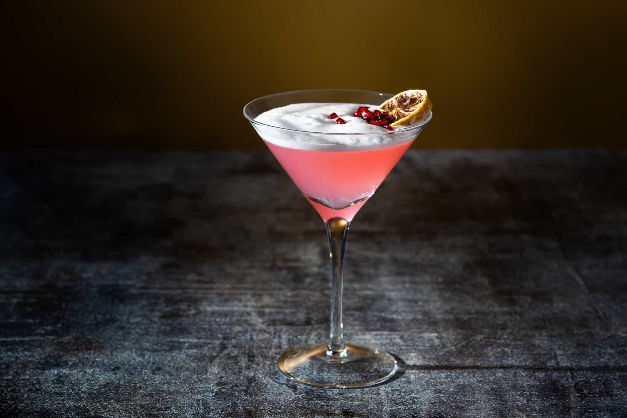 A martini with pomegranate garnish and whipped cream.
