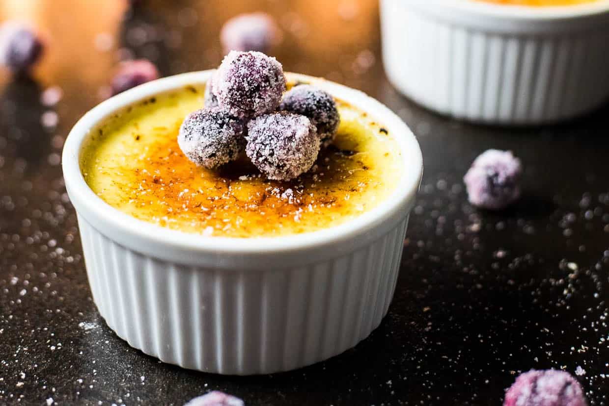 A serving of eggnog creme brulee with sugared cranberries on top.