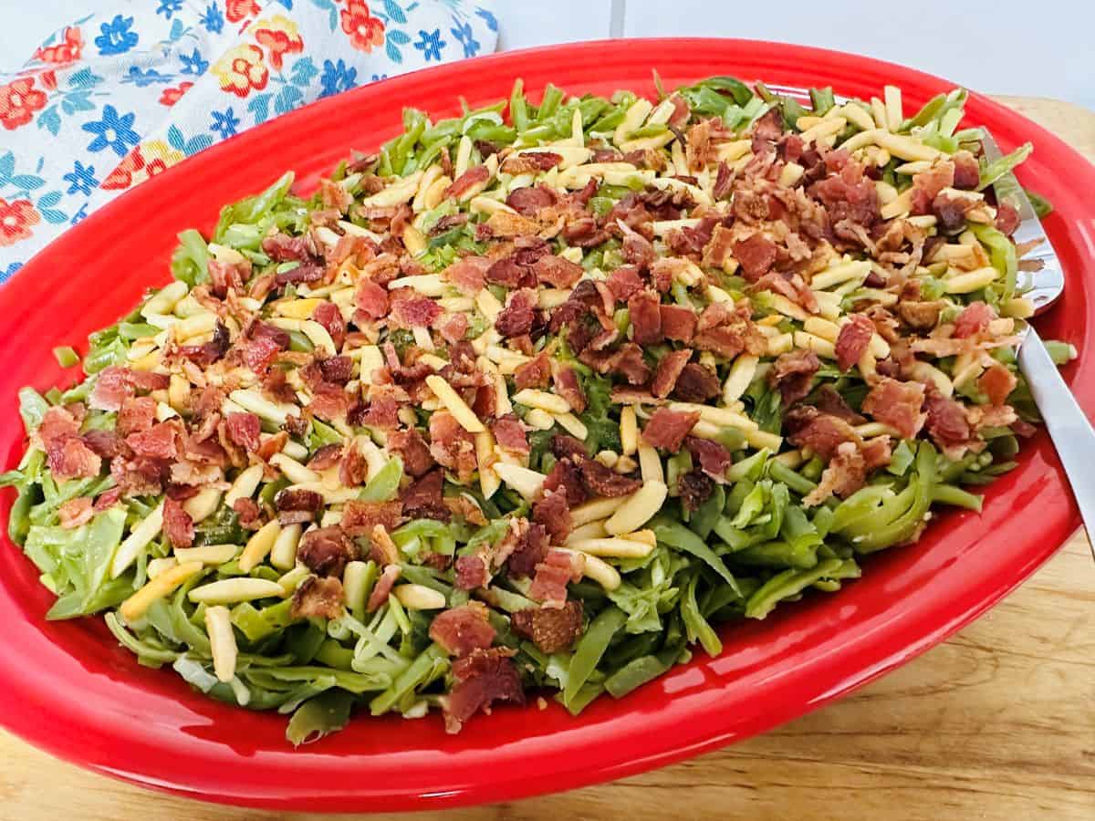 Green beans with bacon and almonds on a red plate.