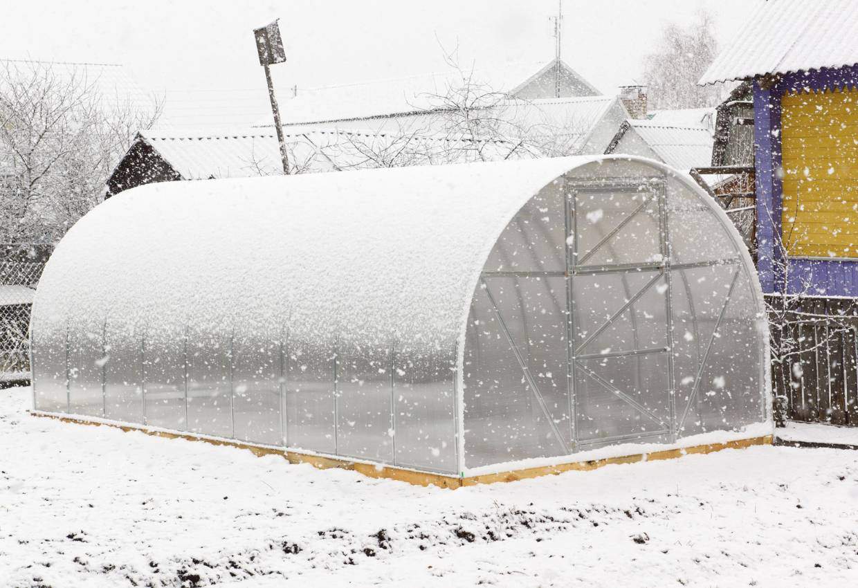 A high tunnel greenhouse covered in snow on a snowy day.