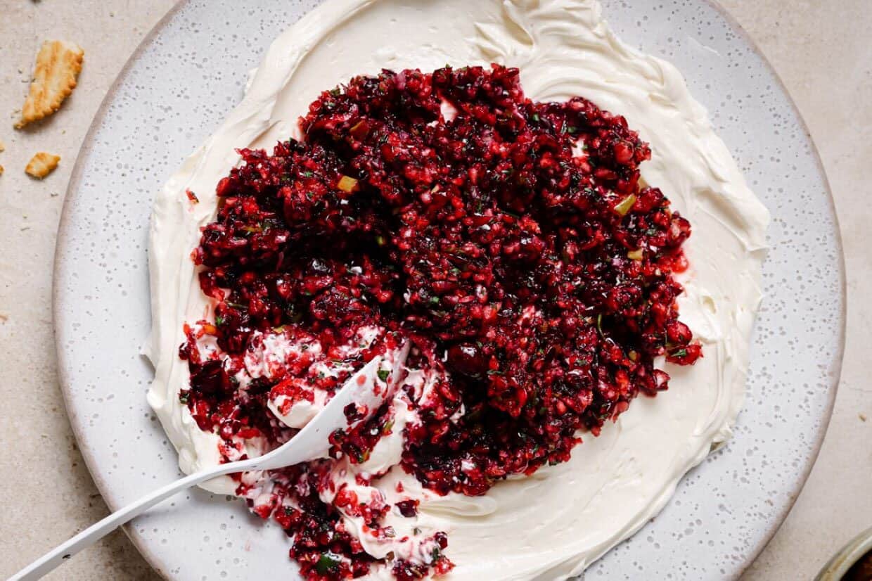 A cracker being dipped into a dish of jalapeño cranberry dip.