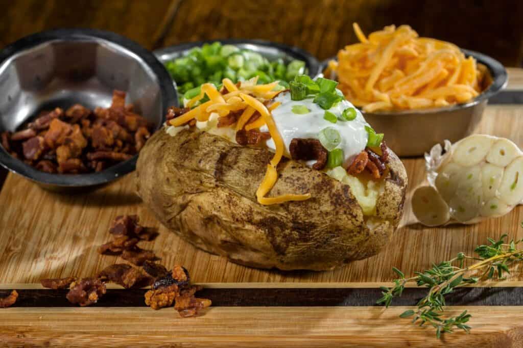 A baked potato on a wooden cutting board with toppings.
