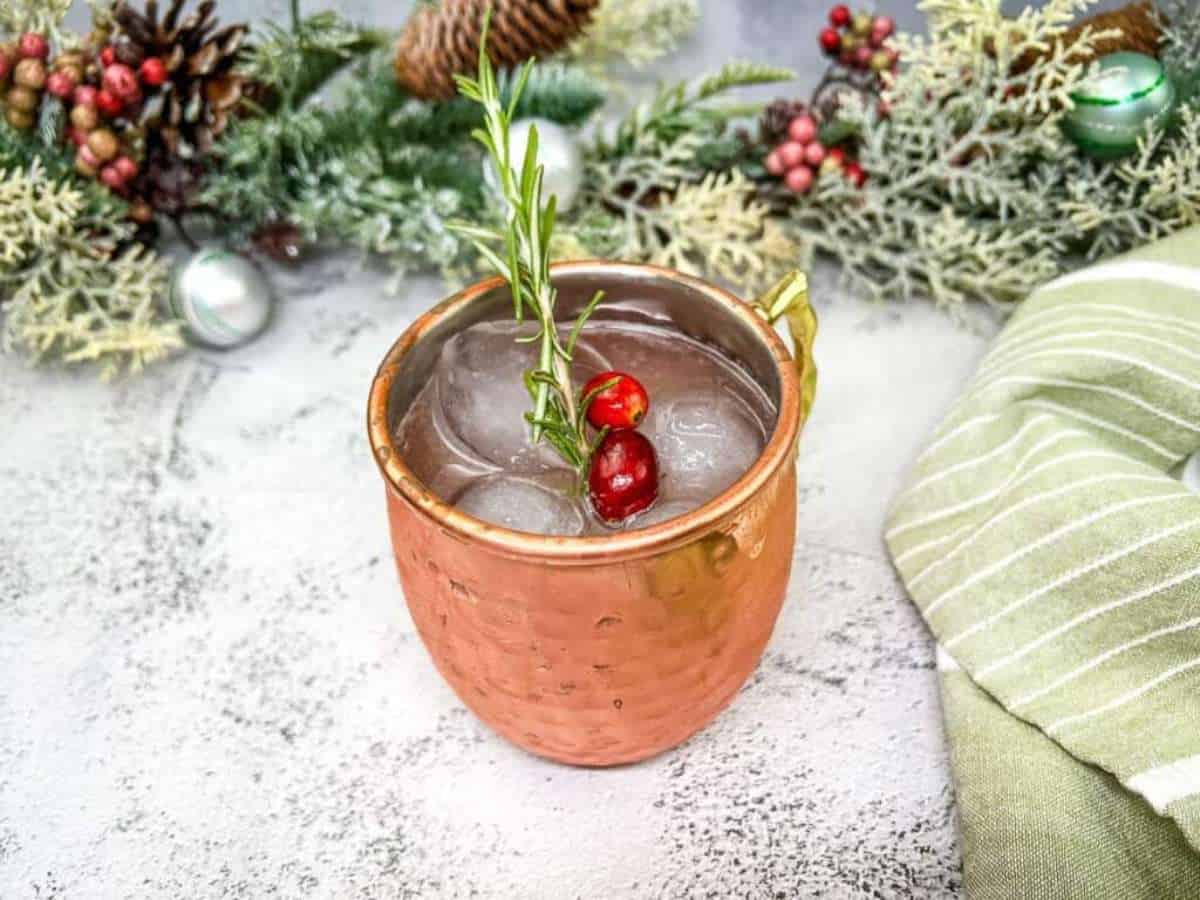 A copper glass filled with mule and with cranberries and a sprig of rosemary.