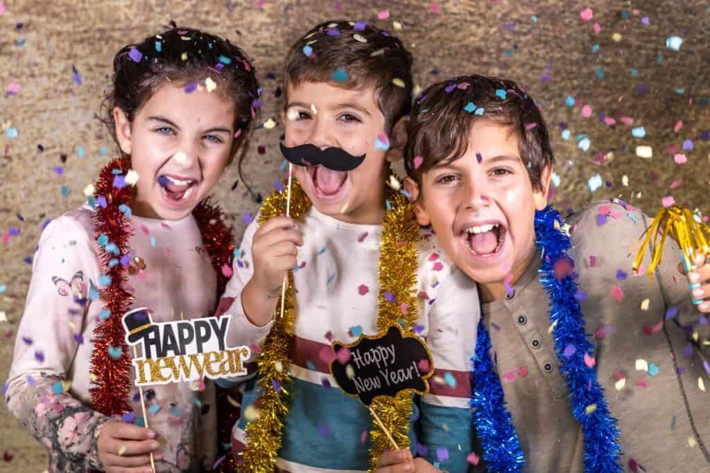 A group of kids holding confetti and a happy new year sign.