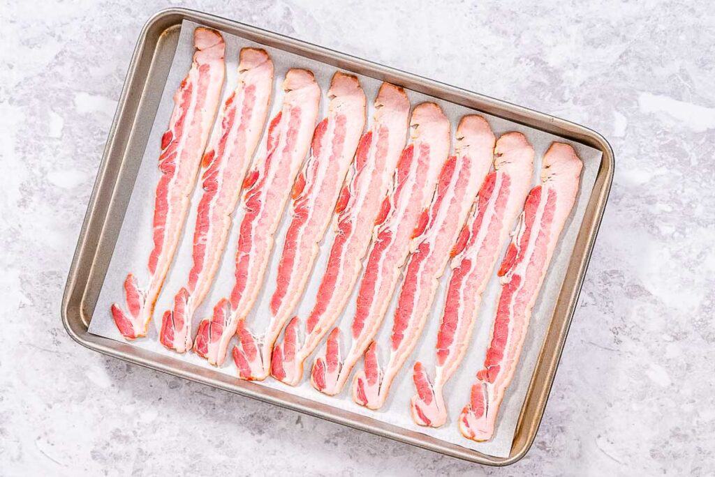Bacon strips on a baking sheet, ready to go in the oven.