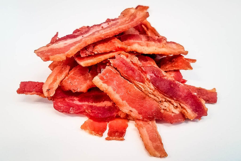 Oven-baked bacon piled on a white surface.