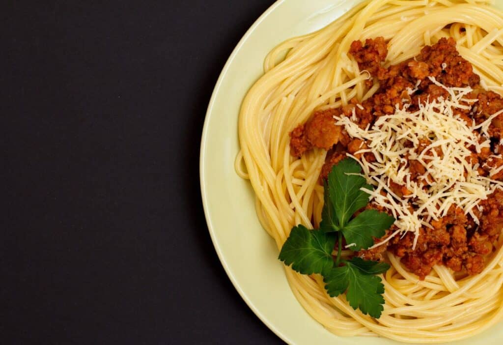 Image shows Spaghetti with meat sauce and parmesan cheese on a plate.