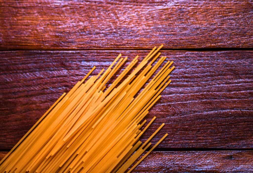 Image shows A bunch of spaghetti on a wooden table.