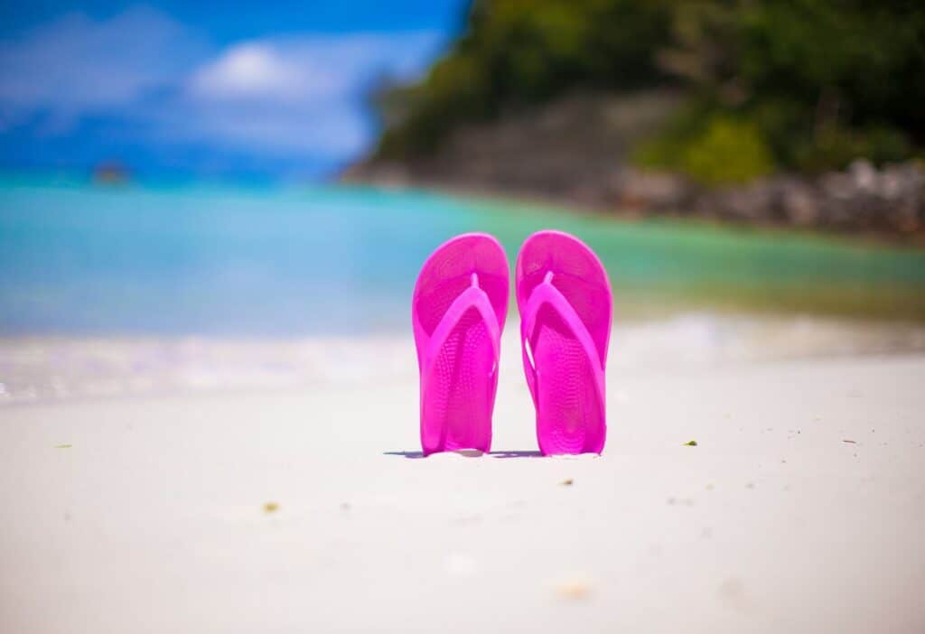 A pair of pink flip flops on a sandy beach.