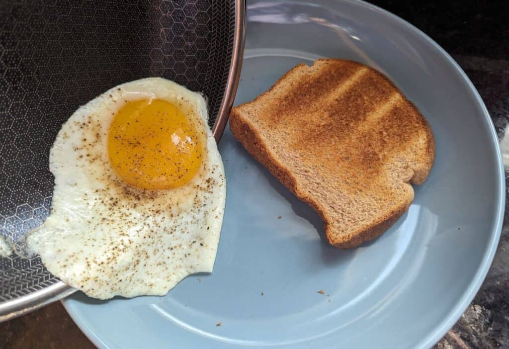 Image shows An egg being slide form a pan to a plate next to a piece of toast.