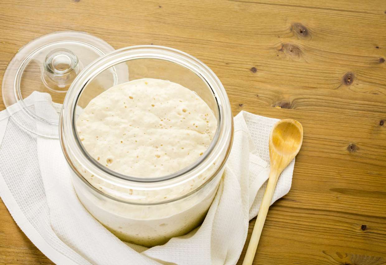 Sourdough starter in a glass jar with a spoon sitting on a wooden table.
