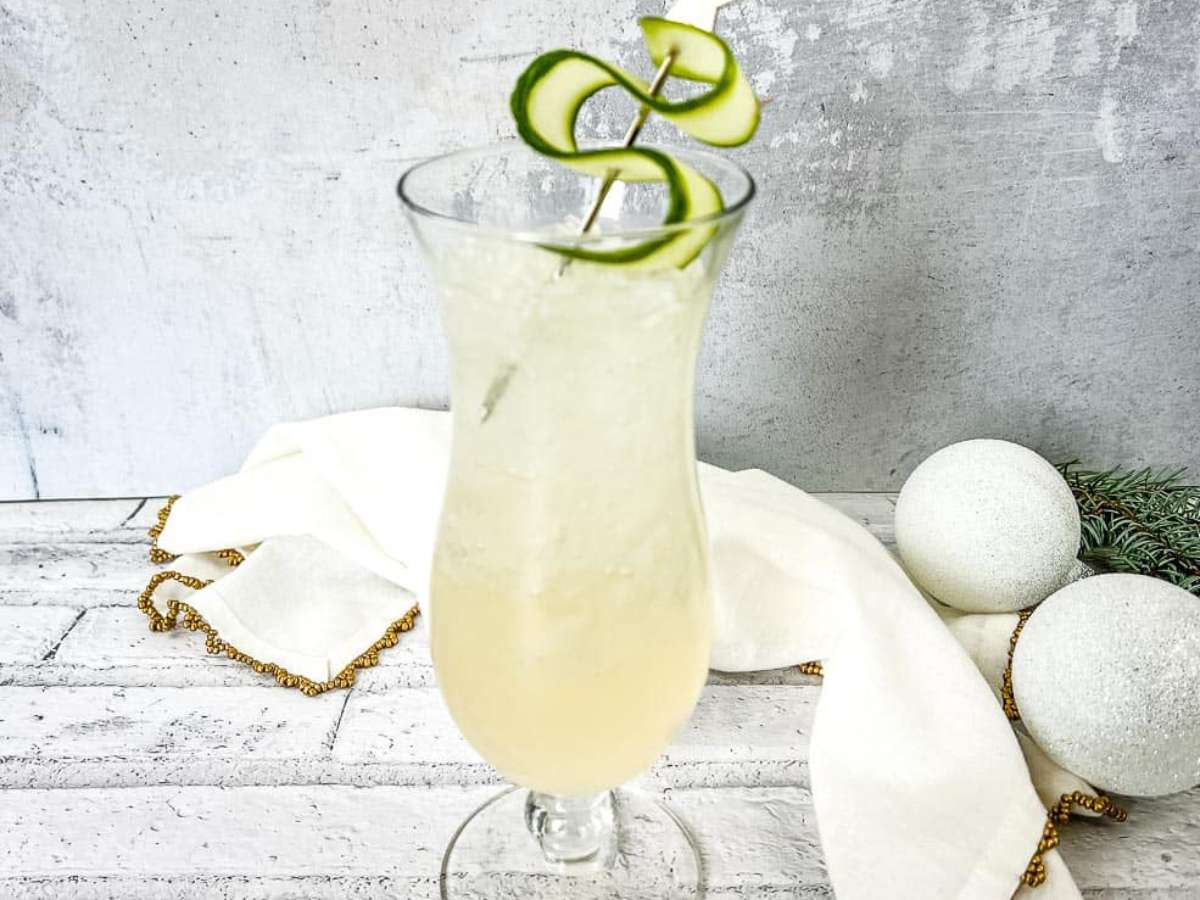 A cocktail with a cucumber garnish on a table.