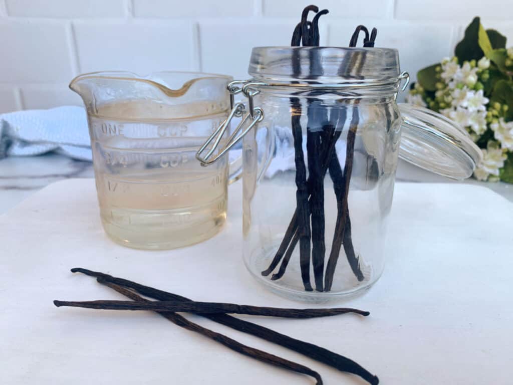 Vanilla beans in a glass jar next to a measuring cup of water.