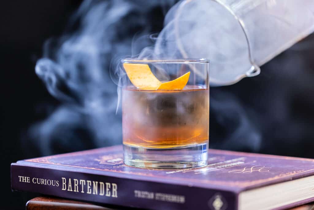 A glass of smoking whiskey sitting on top of a book.