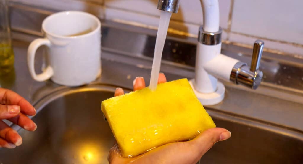 A person is washing a yellow sponge in a sink.
