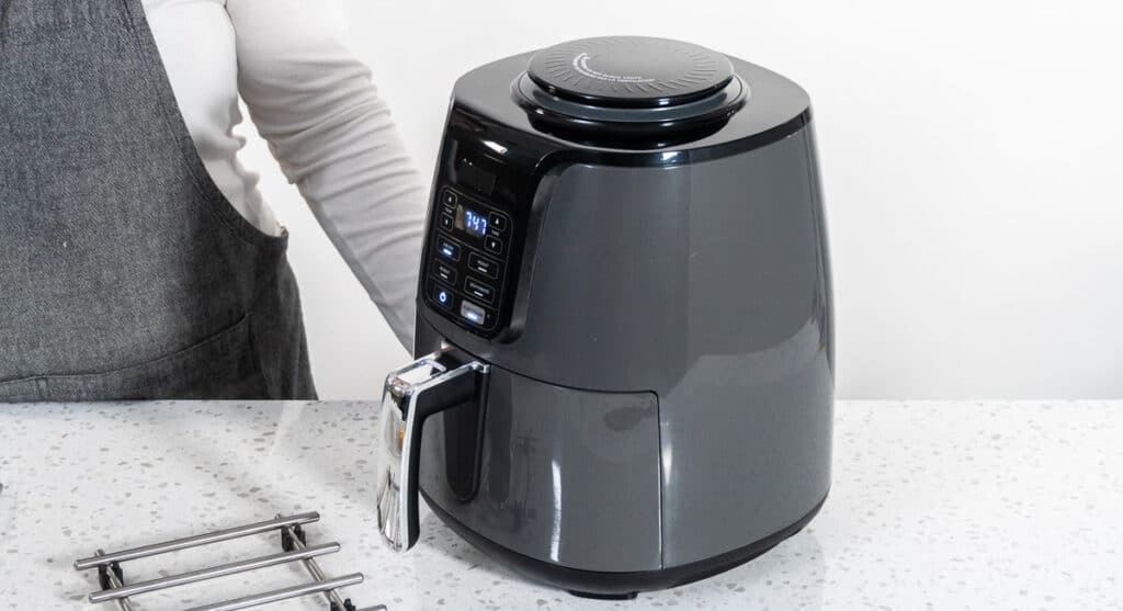 A woman is standing next to an air fryer.