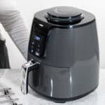A woman is standing next to an air fryer.
