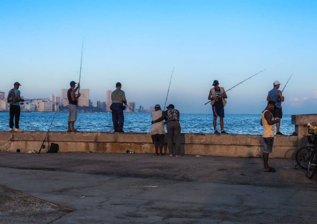 A group of people standing on a pier with fishing poles.