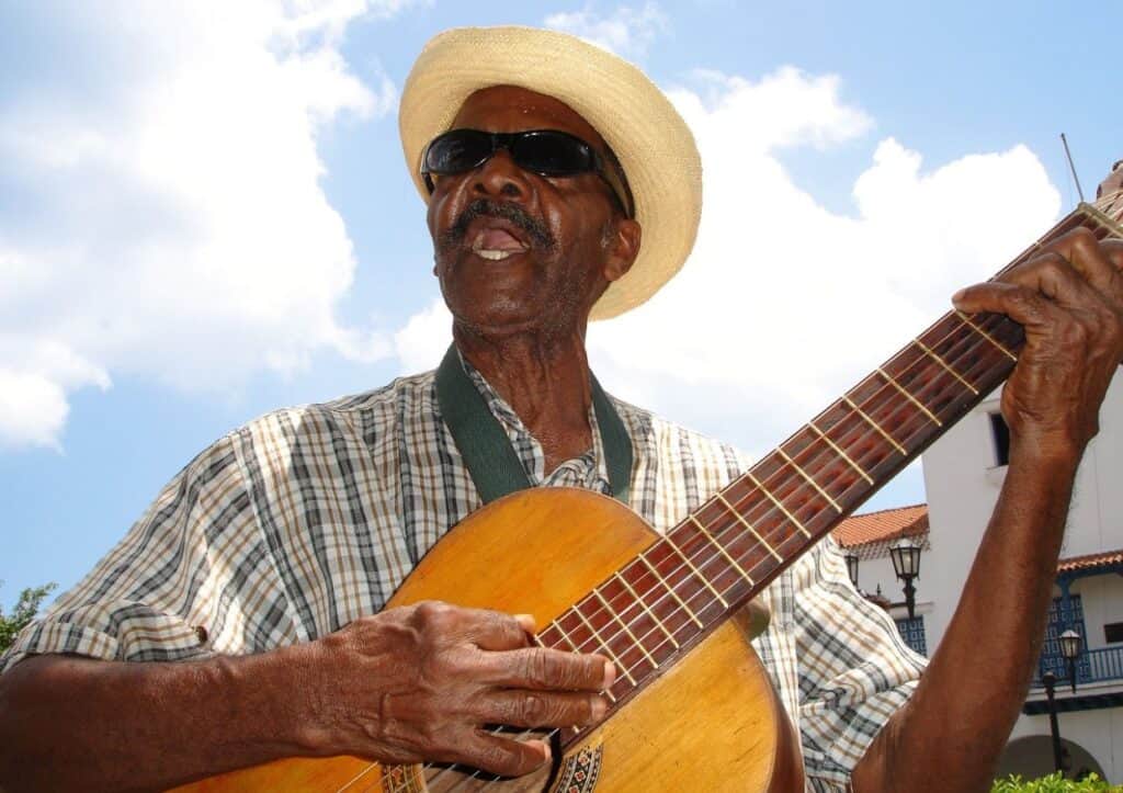 A man wearing a hat and sunglasses is playing a guitar.