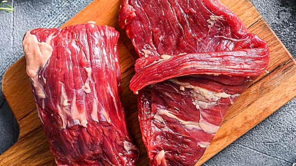 Two raw skirt steak cuts, known as foods high in collagen, rest on a wooden cutting board, showcasing their coarse grain and marbled texture.