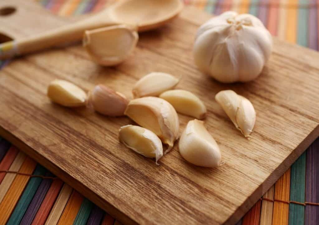 Garlic on a cutting board with a wooden spoon.