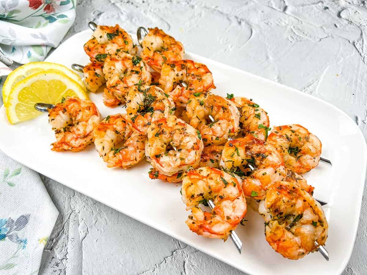 Shrimp skewers on a white plate with lemon wedges.