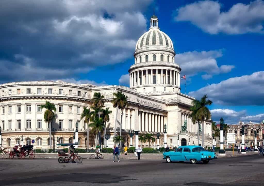 A blue car is parked in front of the capitol building in havana.