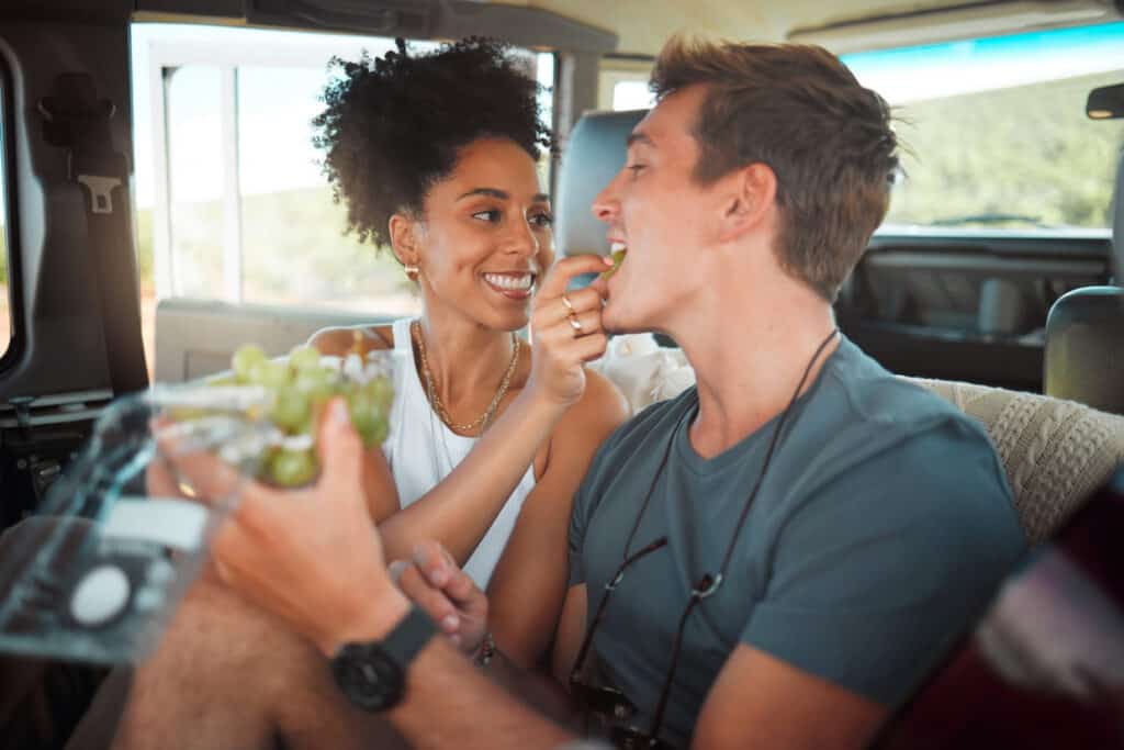 A couple sitting in the back seat of a car enjoying healthy snacks.