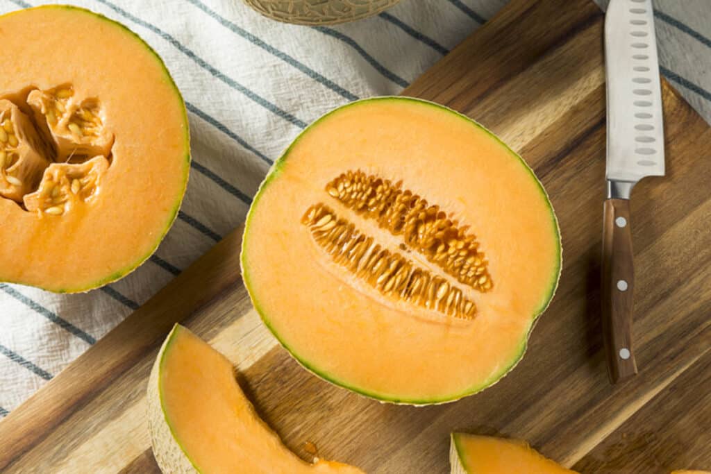 Cantaloupe on a cutting board with a knife.