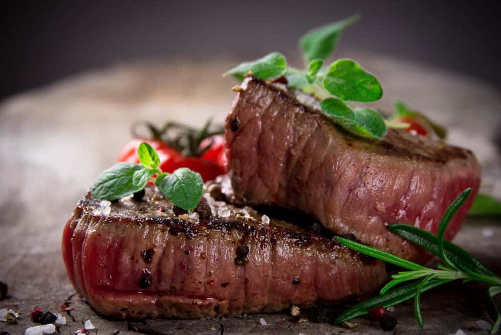 Grilled steak with tomatoes and herbs on a wooden table.