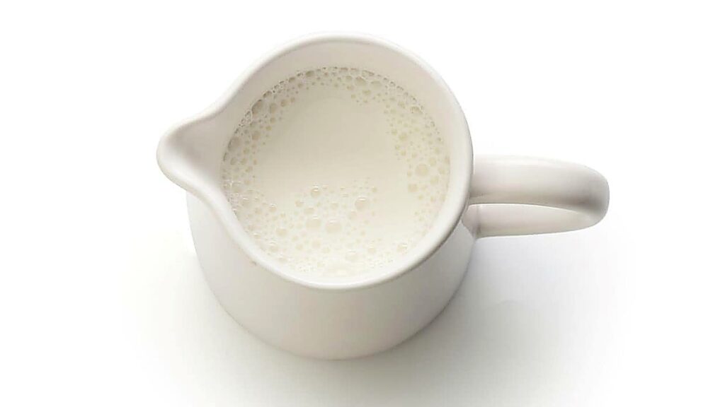 A white ceramic pitcher filled with milk, viewed from above against a white background&mdash;perfect for showcasing evaporated milk substitutes in any kitchen setting.