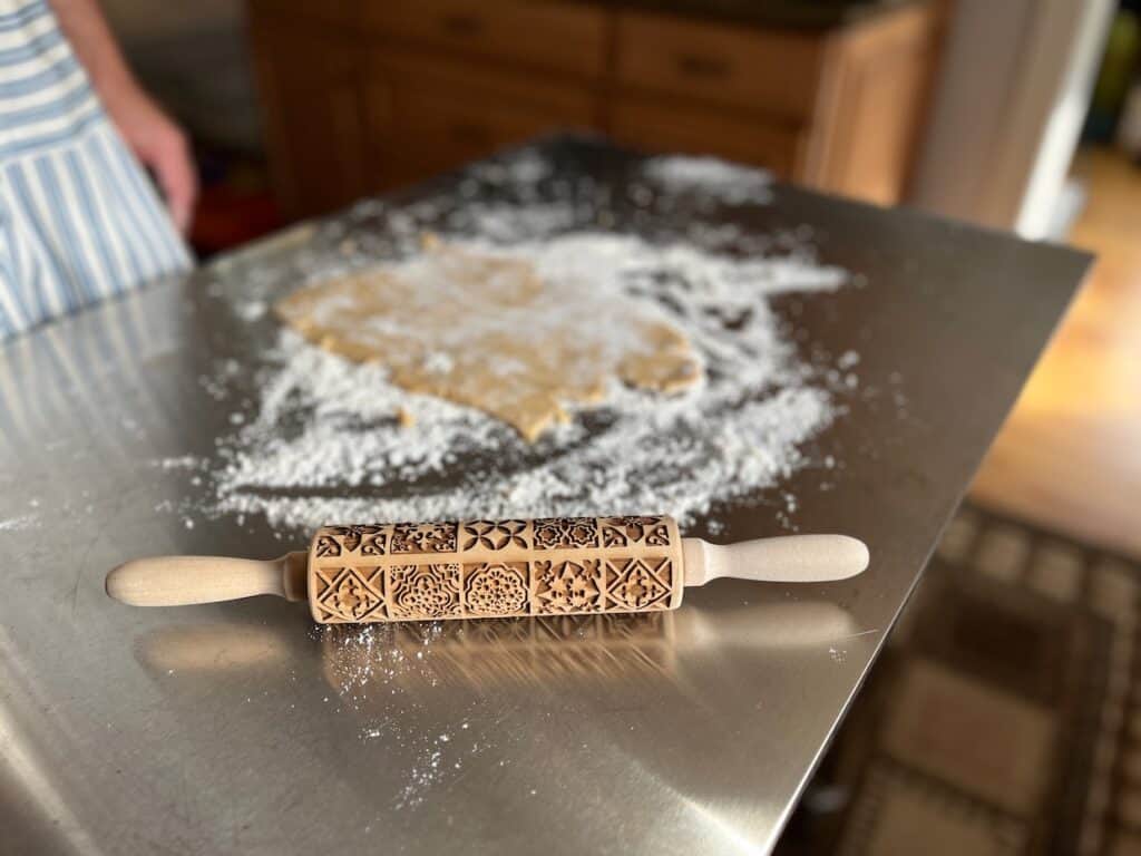 An embossed wooden rolling pin with flour on it.