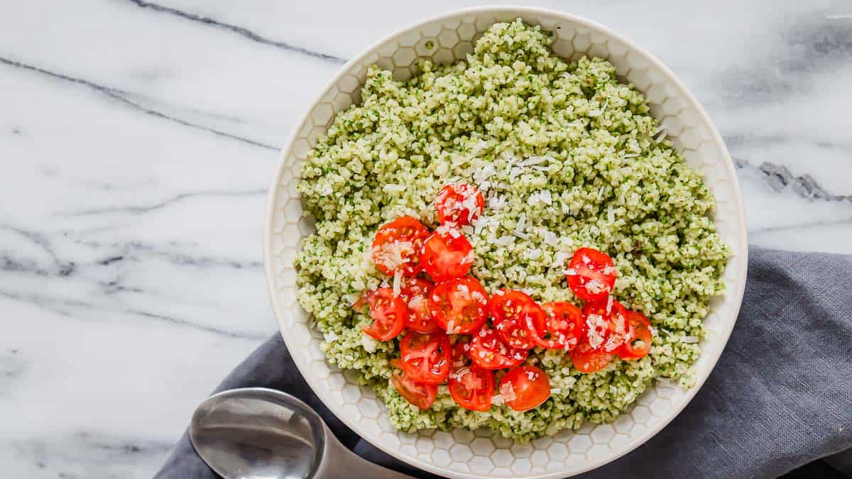 A bowl of pesto couscous with tomatoes and basil.