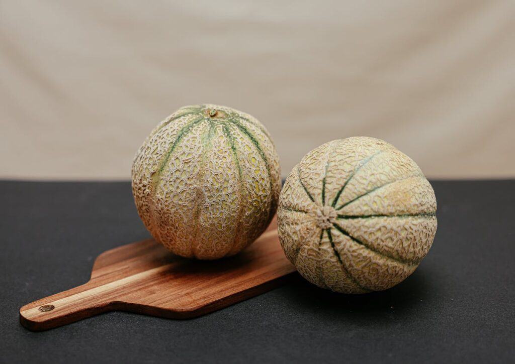 Two melons sitting on top of a wooden cutting board.