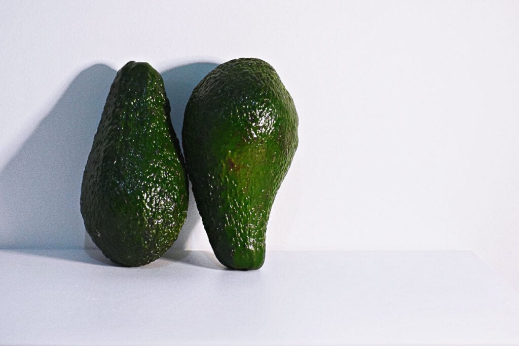 Two avocados on a white surface.